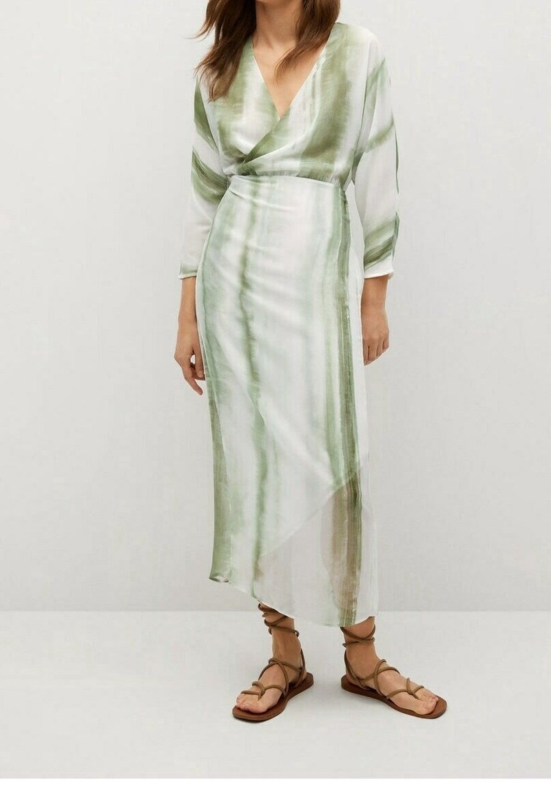Femme portant une longue robe portefeuille à rayures vert clair et blanc avec des manches trois-quarts et des sandales plates marron à lacets.