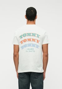 Tricou alb din bumbac, cu text îndrăzneț și multicolor "TOMMY" în diferite stiluri pe spate, iar dedesubt "JEANS New York City".