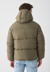 Olivengrøn pufferjakke med hætte, der har et quiltet design, elastiske manchetter og lynlåslukning. Struktureret, isoleret stof.