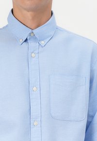 Light blue button-up shirt made of cotton, featuring a collar and a single chest pocket with a subtle texture and white buttons.