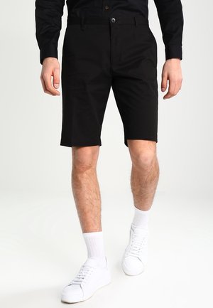Zwarte katoenen shorts met een rechte pasvorm, voorzien van riemlussen, voorzakken en een knoopsluiting, gedragen met witte sneakers.