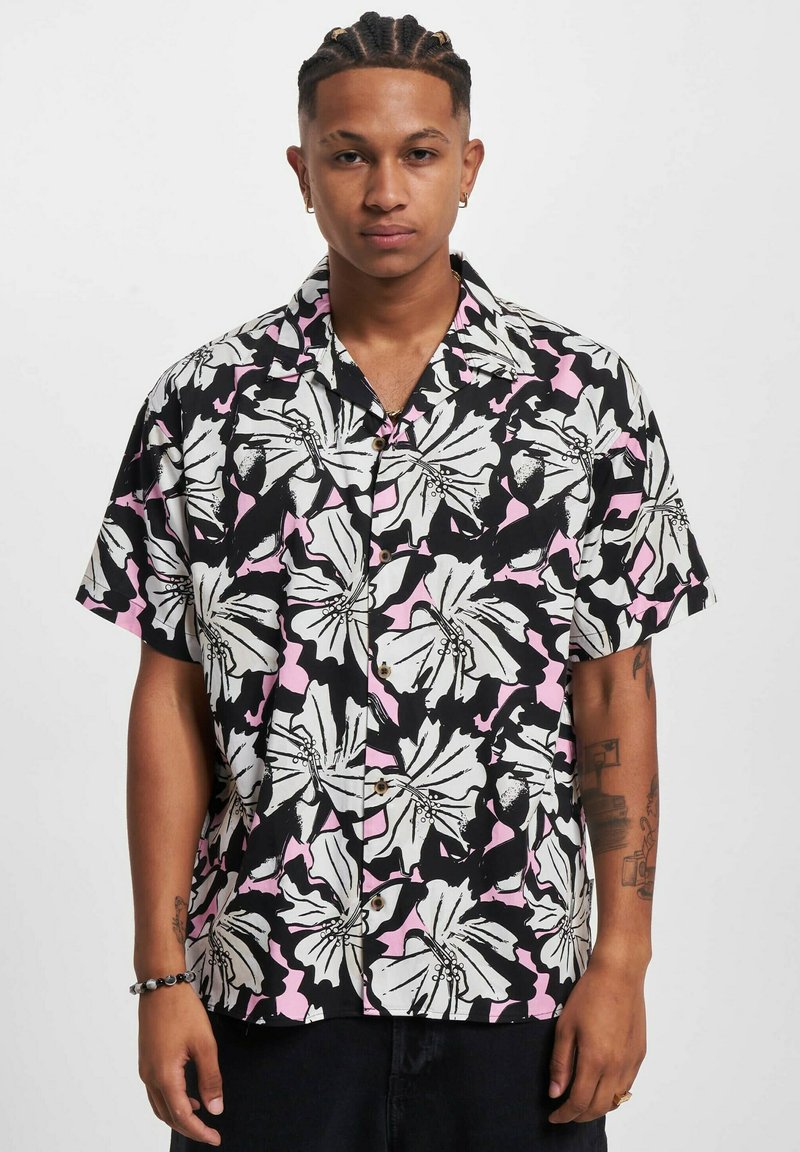 Camisa de manga corta con fondo negro, patrón floral en blanco y rosa, y botones marrones. Hecha de una tela ligera y texturizada.