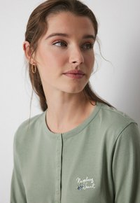 Hellgrünes Langarmhemd mit rundem Halsausschnitt, geknöpftem Vorderteil und floralen Stickereien. Weiches Baumwollmaterial mit feiner Textur.