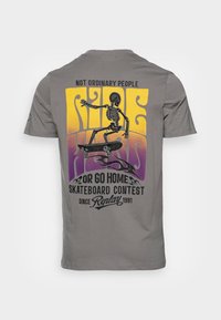 T-shirt en coton gris avec un squelette sur un skateboard et un design de texte coloré. L'impression comprend des accents dégradés violets et jaunes.