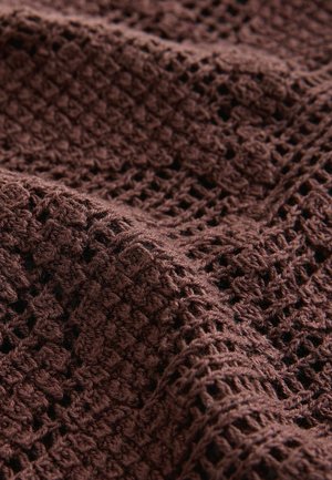 Pruun kootud tekstiil tekstureeritud, avatud mustriga. Riie näitab keerukat heegeldatud mustrit, millel on pehme, kiuline välimus.