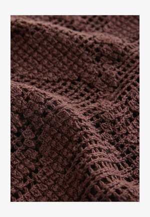 Barna szövött textília texturált, nyitott mintával. A szövet részletes horgolt mintázatot mutat, lágy, rostos megjelenéssel.