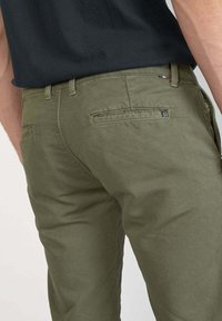 Olijfgroene chino's gemaakt van katoen, met achterzakken, riemlussen en een merklabel op de tailleband, met een zijdezachte textuur.