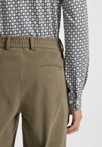 Khaki corduroy broek met een gestructureerde stof en slim fit, met een achterzak en een rekbare tailleband, gecombineerd met een geometrisch patroon overhemd.