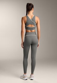 Szary zestaw sportowy składający się z biustonosza sportowego z krzyżowanym tyłem i wycięciem oraz legginsów o wysokim stanie. Gładki, elastyczny materiał z kontrastowymi wykończeniami.