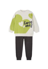 Maglione lavorato a maglia con motivi a cuore verdi e testo "Amami!" su uno sfondo crema, abbinato a pantaloni grigi con texture.