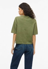 Zielony dziergany sweter z krótkimi rękawami, okrągłym dekoltem i krótkim krojem, zestawiony z ciemnoniebieskimi, wysokim stanem jeansami.