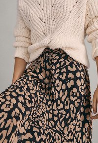 Dikke crème gebreide trui gecombineerd met een zwarte rok met een tan dierenprint, afgewerkt met knopen aan de voorkant.