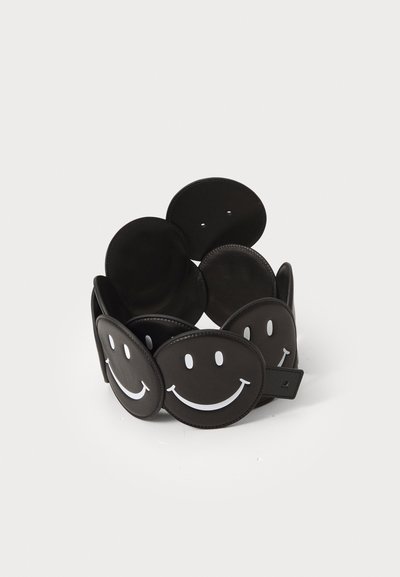 Ceinture en cuir noire avec des panneaux circulaires ornés de motifs de visages souriants blancs. Texture lisse, sangle ajustable et style minimaliste.