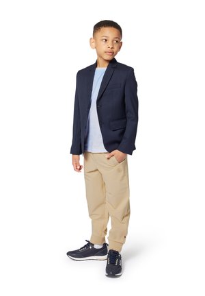 Blazer marine, t-shirt bleu clair, pantalon beige et sneakers marines. Le blazer a une fermeture à un bouton et des poches avant. Tenue décontractée.