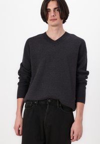 Gråmelert genser med V-hals i myk strikket materiale, med lange ermer og ribbestrikkede mansjetter, kombinert med svarte, løstsittende jeans.
