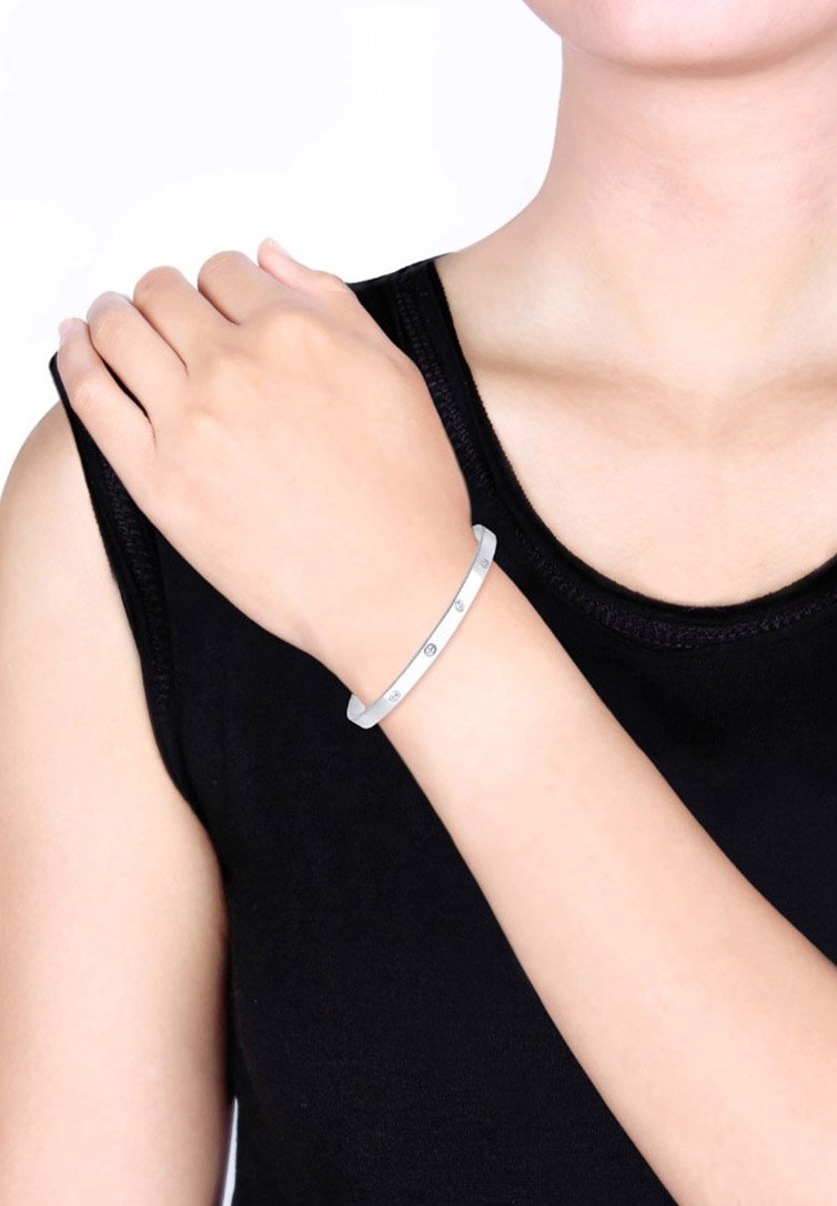 Bracelet en métal argenté avec une surface lisse et polie ; présente cinq petits accents ronds uniformément espacés le long du bracelet. Ajustable.
