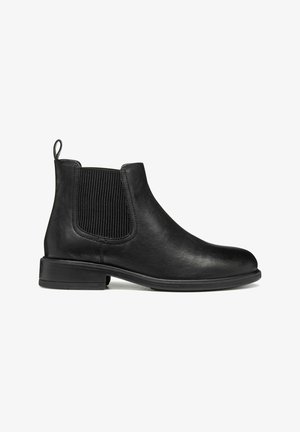 Botín negro de cuero con paneles elásticos a los lados y una pestaña en el talón. Textura suave y puntera redonda sobre un tacón bajo y plano.