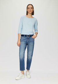Hellblaues Langarmoberteil, denimblau tapered Jeans und weiße klobige Sneakers, dazu ein schwarzer Gürtel mit einer silbernen Schnalle.