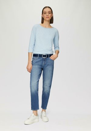 Hellblaues Langarmoberteil, denimblau tapered Jeans und weiße klobige Sneakers, dazu ein schwarzer Gürtel mit einer silbernen Schnalle.