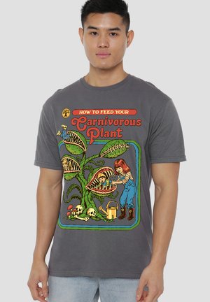 Young woman feeds children trapped in large Venus flytrap plants with skulls and bones nearby on a gray shirt.