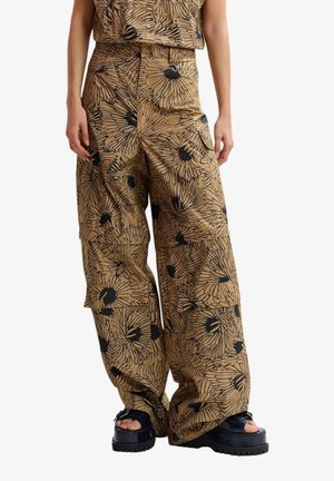 Pantaloni ampi color sabbia con stampa floreale astratta nera, indossati con sandali neri con plateau, visibili dalla vita ai piedi.