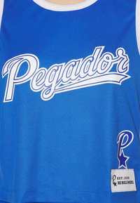 Modrý síťovaný top s ramínky s nápisem "Pegador" bílým písmem, malou nášivkou a bílým lemem kolem výstřihu a průramků.