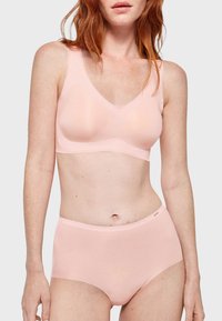 Draadloze bralette en hoog-geknipte slips van zacht, lichtroze stof. Gladde textuur, minimalistisch ontwerp, met een subtiel logo op de tailleband.