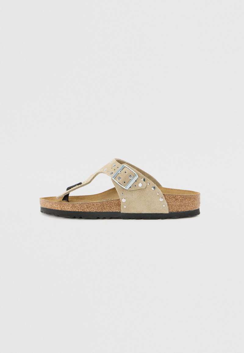Beige suède flip-flop sandalen met kurken voetbed, zwarte rubberen zool, metalen gesp en zilveren studs langs de band.