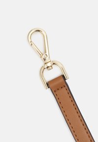 Tannenkleurige lederen band met een goudkleurige draaiklem. Het leer heeft een gladde textuur en zichtbare stiksels langs de randen.