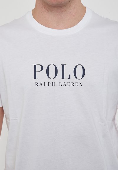 T-shirt in cotone bianco con scollatura a girocollo. La parte frontale presenta la scritta blu marina: "POLO RALPH LAUREN" in grassetto, maiuscolo. Maniche corte.