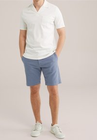 Vit kortärmad pikétröja med V-ringning och en bröstficka, kombinerad med ljusblå shorts och vita sneakers.