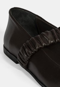 Dunkelbraunes Leder-Schuhwerk mit einem gerafften Textur an der Oberseite, glatter Oberfläche und einer niedrigen schwarzen Sohle.