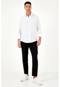 Fehér gombos ing textúrált anyagból, felgöngyölt ujjak, fekete slim fit nadrággal és fehér sportcipővel párosítva.