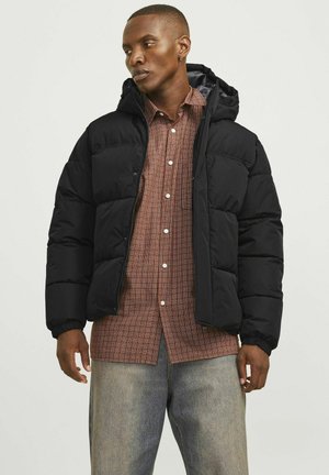 Black puffer jacket with a hood, quilted design, elastic cuffs, and front zip. Layered over a checkered shirt, paired with light jeans.