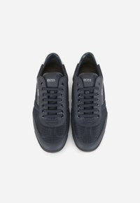 Mörkblå sneakers i mesh och lädermaterial, med runda skosnören, perforerat mönster och en logotyp på tungan.