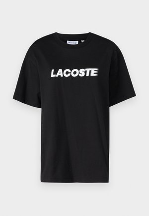 Svart bomulls T-skjorte med hvit trykket "LACOSTE" logo på framsiden. Korte ermer og rund hals. Klassisk avslappet passform.