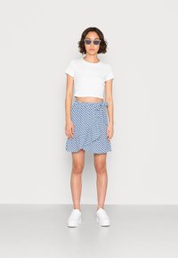 Camiseta curta branca combinada com uma saia envolvente azul e branca às riscas, com um detalhe de laço, finalizada com ténis de plataforma brancos.