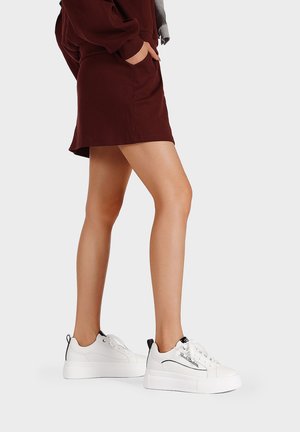 Sneaker platform bianche con dettagli neri e cuciture laterali, abbinate a un vestito bordeaux. Le sneaker sono dotate di lacci e di una suola testurizzata.