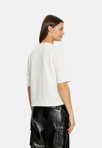 Witte katoenen t-shirt met korte mouwen en een ronde halslijn, vanuit de achterkant bekeken, gecombineerd met zwarte leren cargobroek.