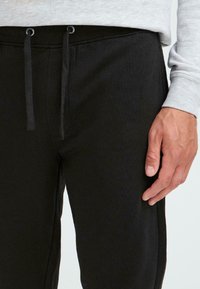 Schwarze Sweatpants mit elastischem Bund, Kordelzug und seitlichen Taschen, ausgestattet mit einer weichen Textur und schmalem Schnitt.