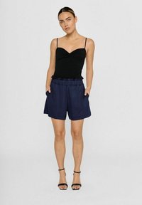 Schwarzes enges Tanktop mit dünnen Trägern, kombiniert mit marineblauen Shorts, die einen elastischen Bund und seitliche Taschen haben.