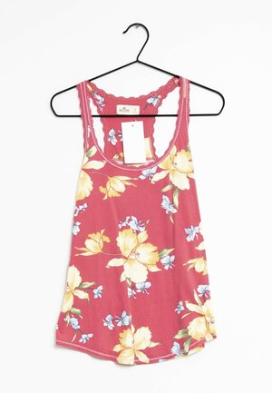 Top de tirantes floral rosa con flores amarillas y azules, con espalda de encaje, colgando de una percha negra con una etiqueta blanca.