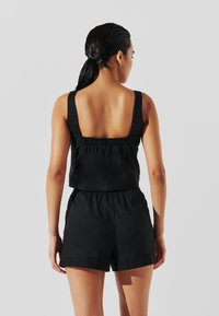 Haut sans manches noir avec un dos carré et un élastique froncé à la taille, associé avec un short noir assorti. Texture de tissu lisse.