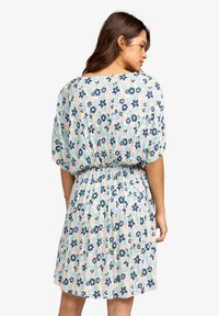 Bloemenjurk in pastelkleuren, met korte mouwen, een elastische taille en een print van blauwe en roze bloemen op een lichte achtergrond.