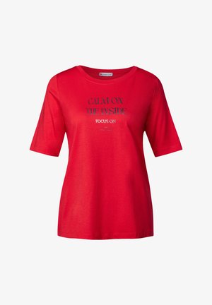 T-shirt rouge à manches courtes, col rond, avec un texte imprimé : "CALME À L'INTÉRIEUR, FOYER SUR". Matière en coton doux, coupe décontractée.