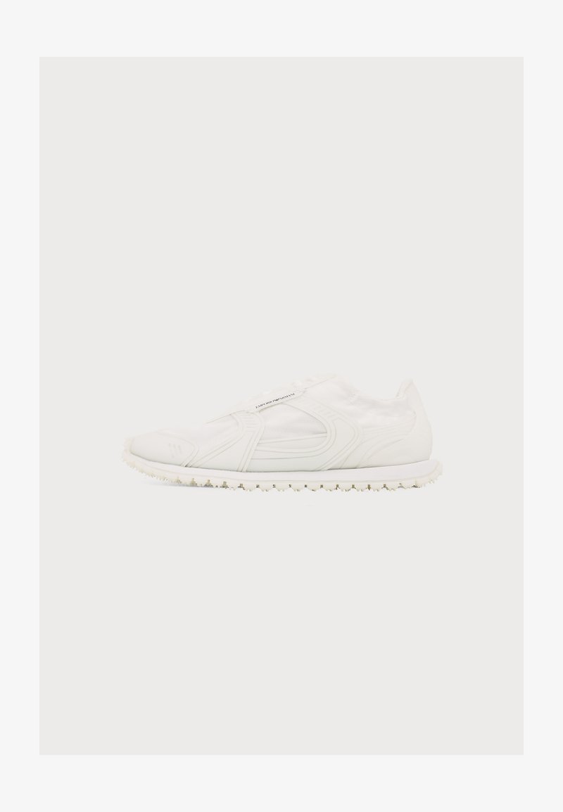 Baskets slip-on entièrement blanches avec semelle texturée et détails subtils sur les côtés et le dessus sur un fond blanc uni.