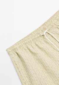 Pantaloni corti verde chiaro con un motivo ondulato bianco, cintura elastica e chiusura con cordino. Il tessuto ha un aspetto morbido e texturizzato.