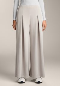 Wijde broek van lichtgrijs stof, met voorplooien en een gladde textuur, gecombineerd met witte sneakers.