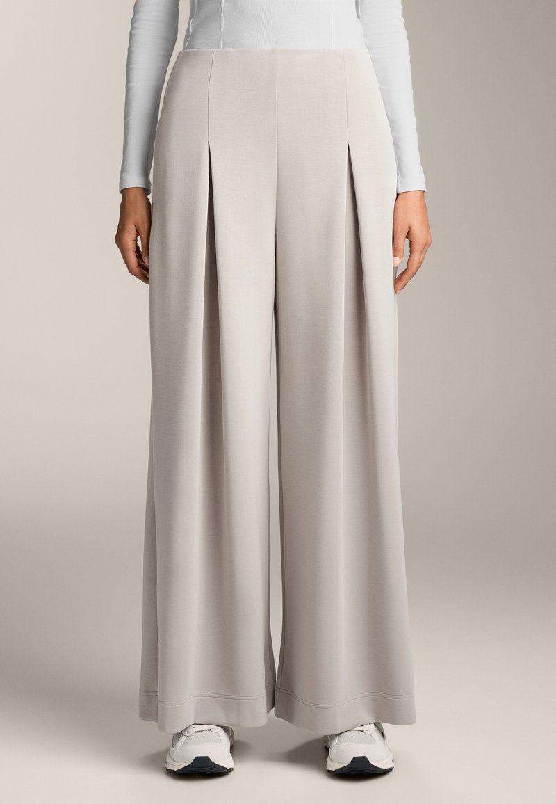 Wijde broek van lichtgrijs stof, met voorplooien en een gladde textuur, gecombineerd met witte sneakers.