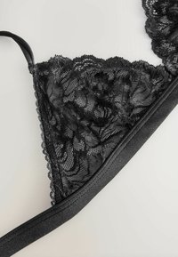 Zwarte kant bralette met bloemenpatronen, gekartelde randen en een gladde zwarte band. Zachte textuur met ondersteuning door onderdraden.